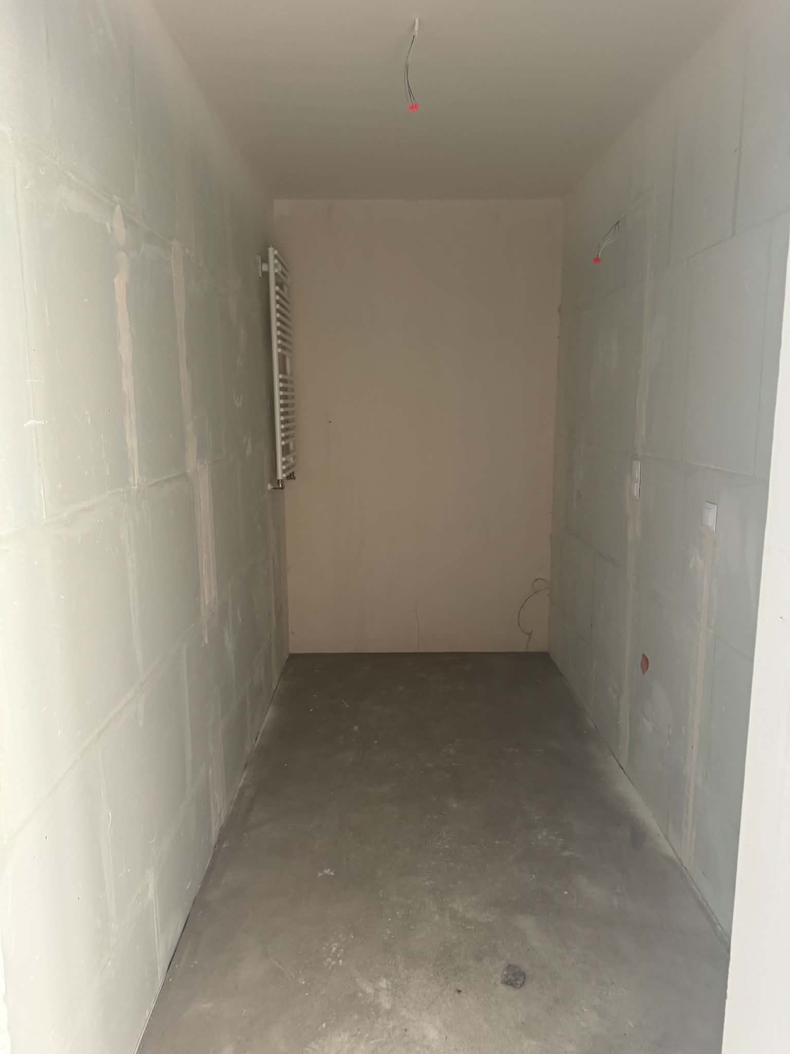 Bathroom at developer standard: plasterboard walls, bare screed floor, a ladder radiator on the wall.