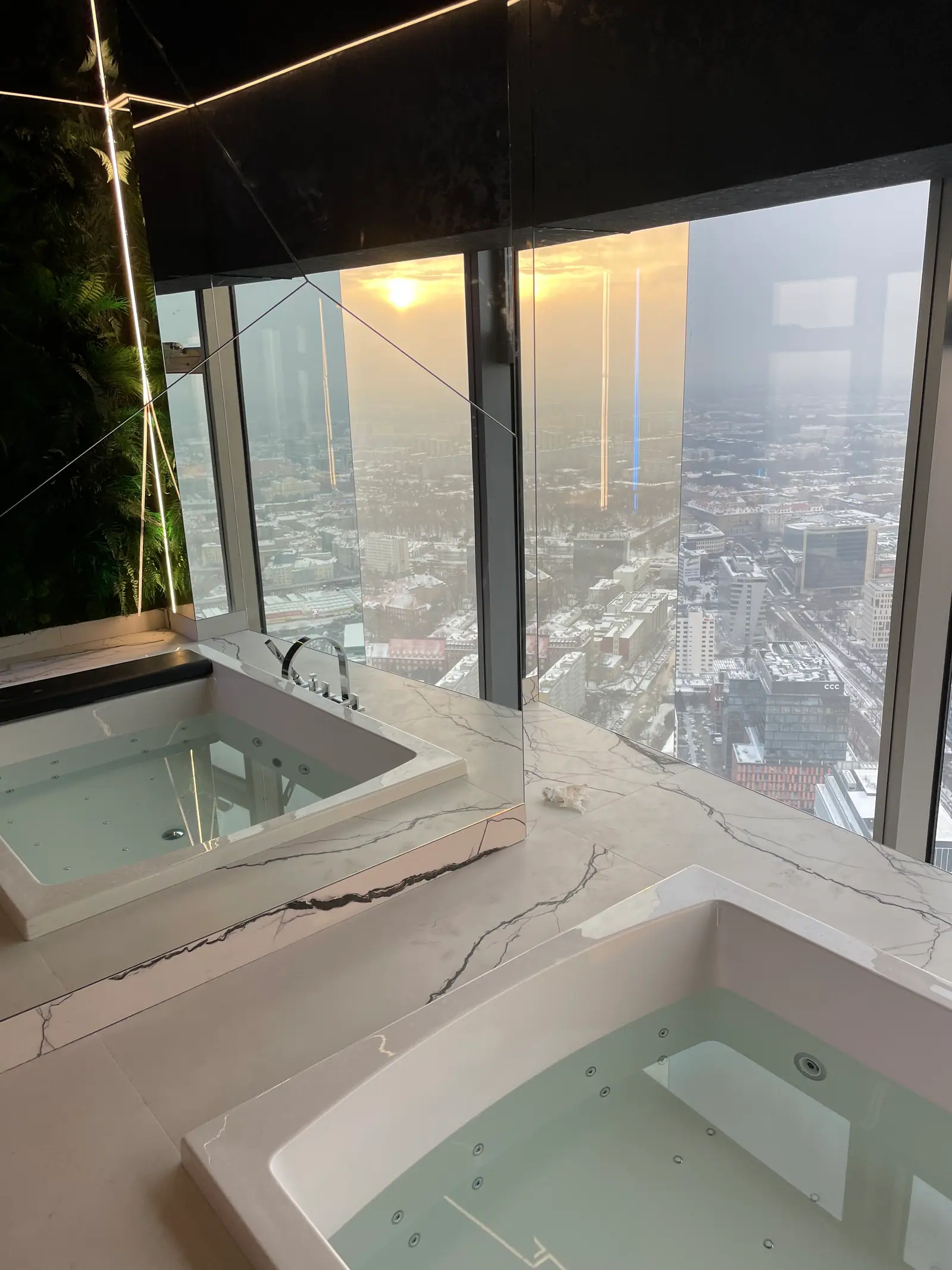 Two whirlpool bathtubs in a light marble-patterned surround, with the city skyline behind the glass.