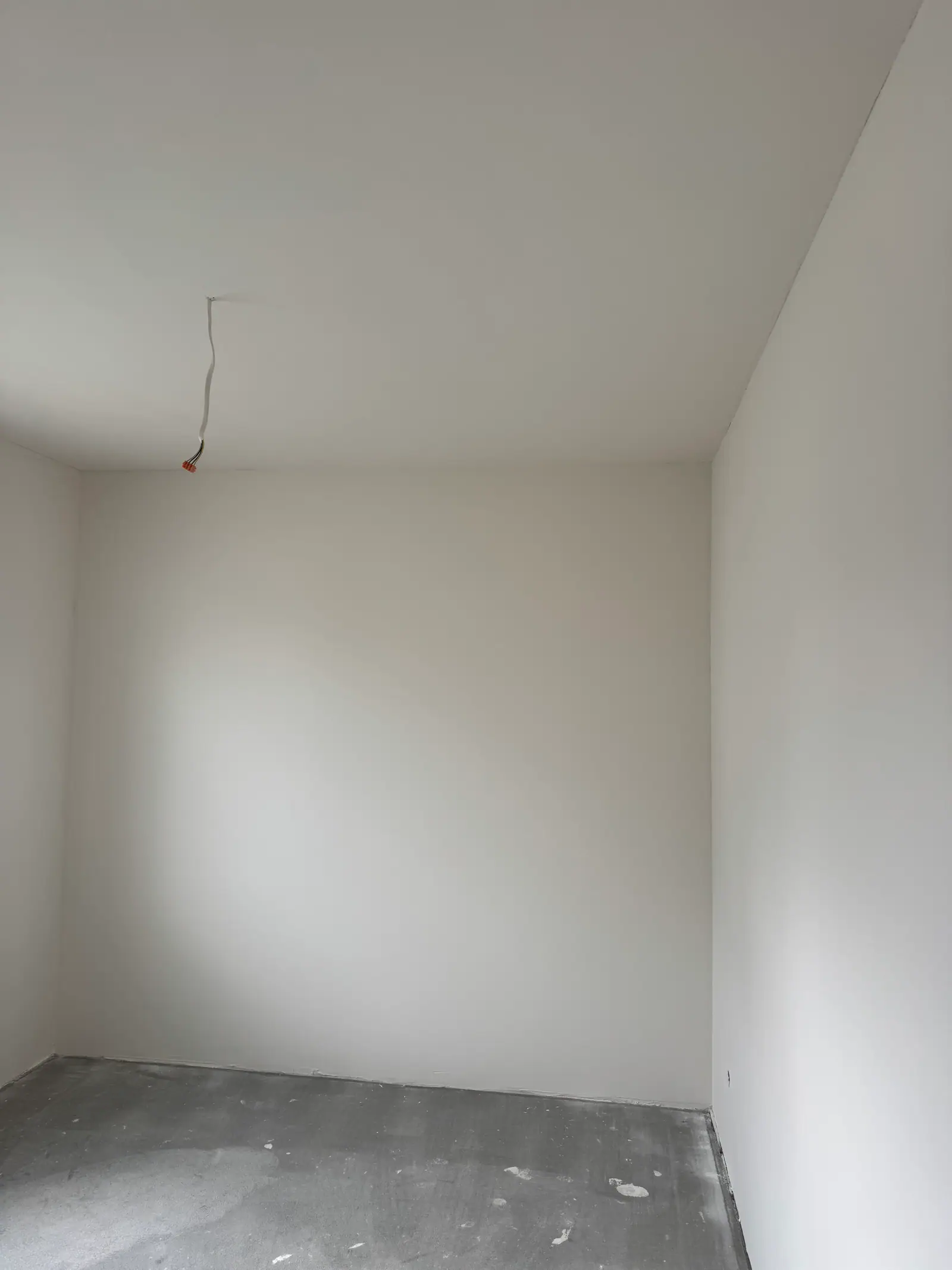 The corner of an empty room: smooth white walls and ceiling, a bare screed floor.