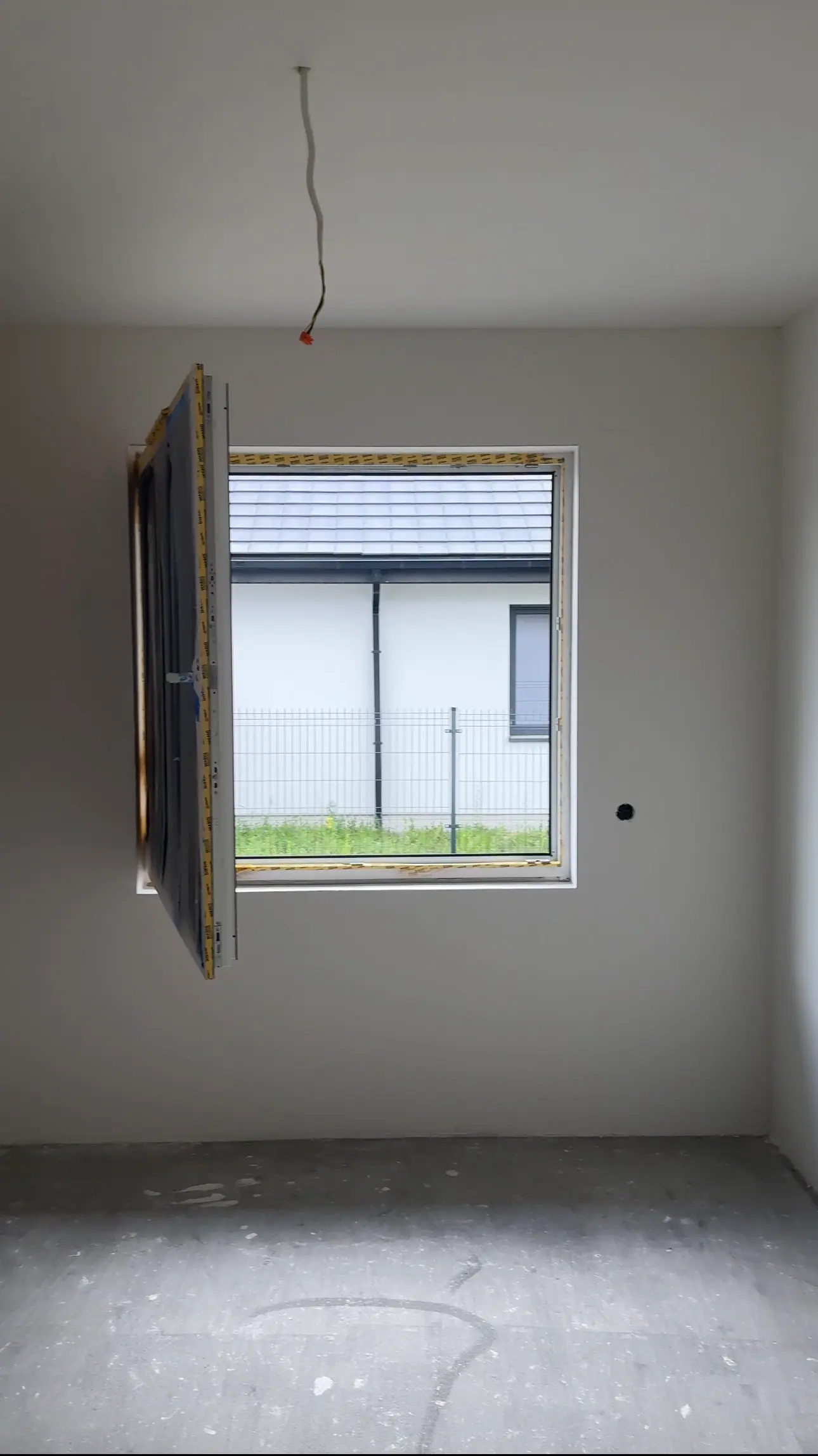 A room with smooth white walls and an open window, with a bare screed floor.