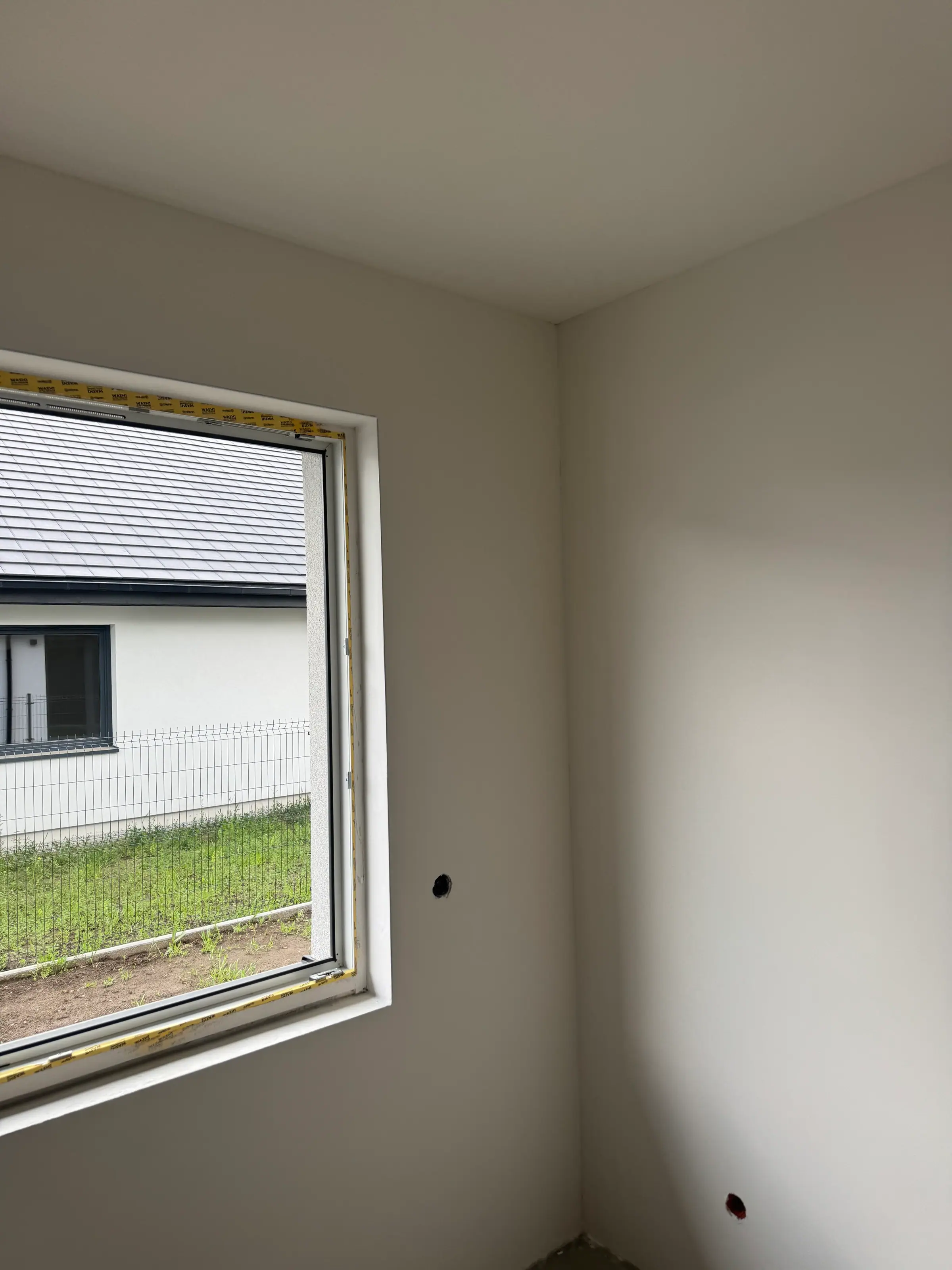 An empty room with smooth white walls and ceiling, and a window looking onto a neighbouring building.