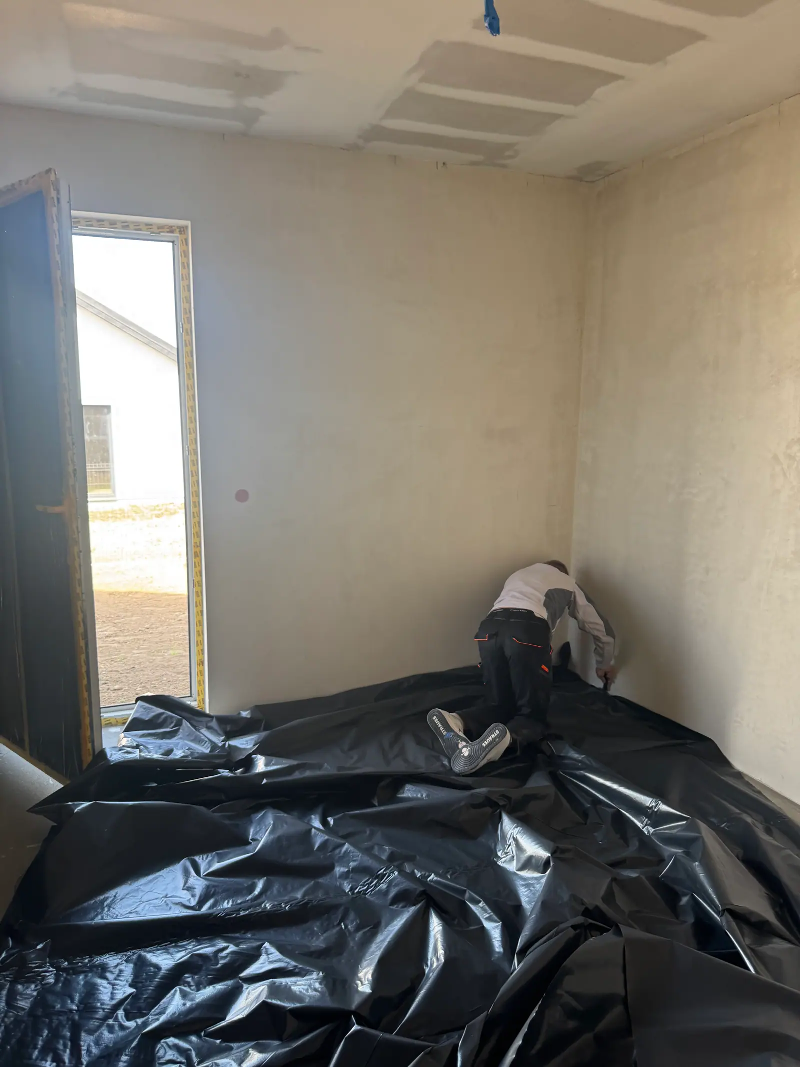 A worker lays black protective film on the floor of a room.