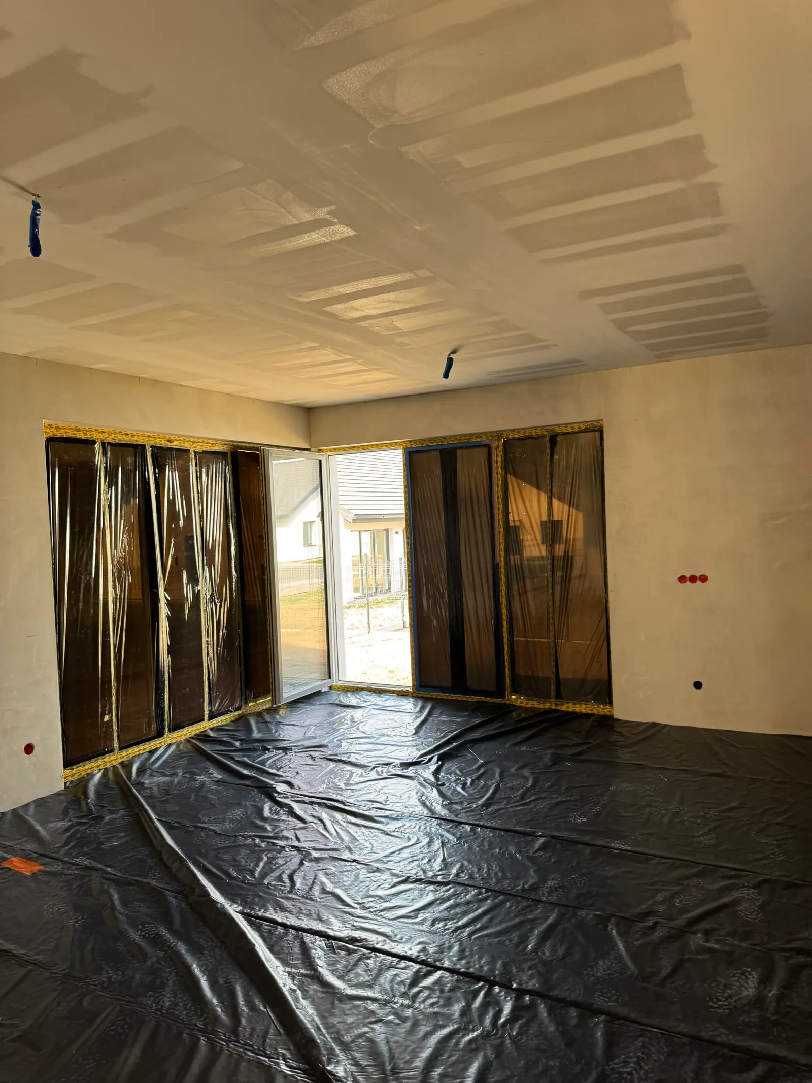 A large room during the work: filled joints on the ceiling, windows and floor protected with film.