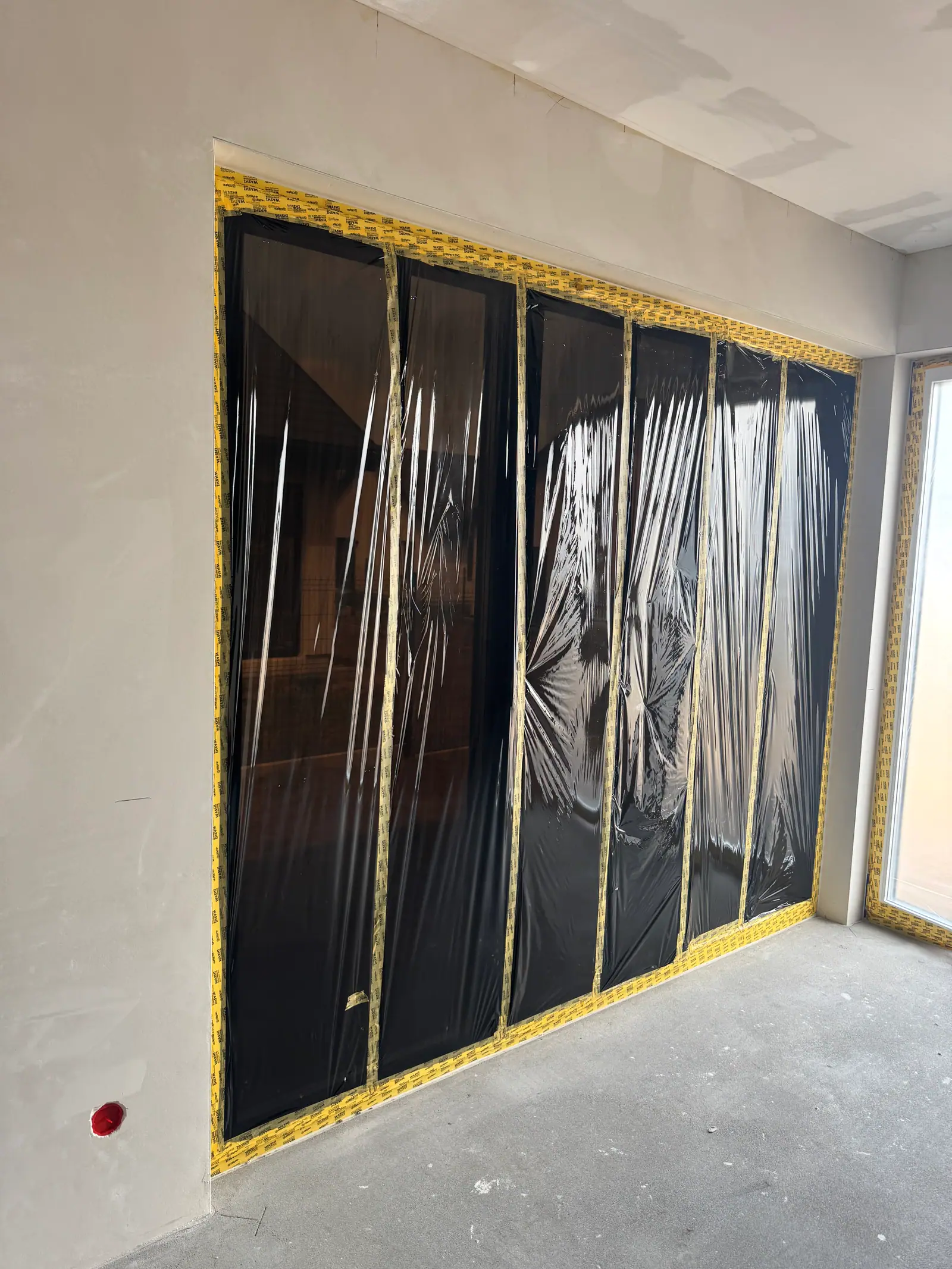 A large glazed wall covered with protective film and yellow tape.
