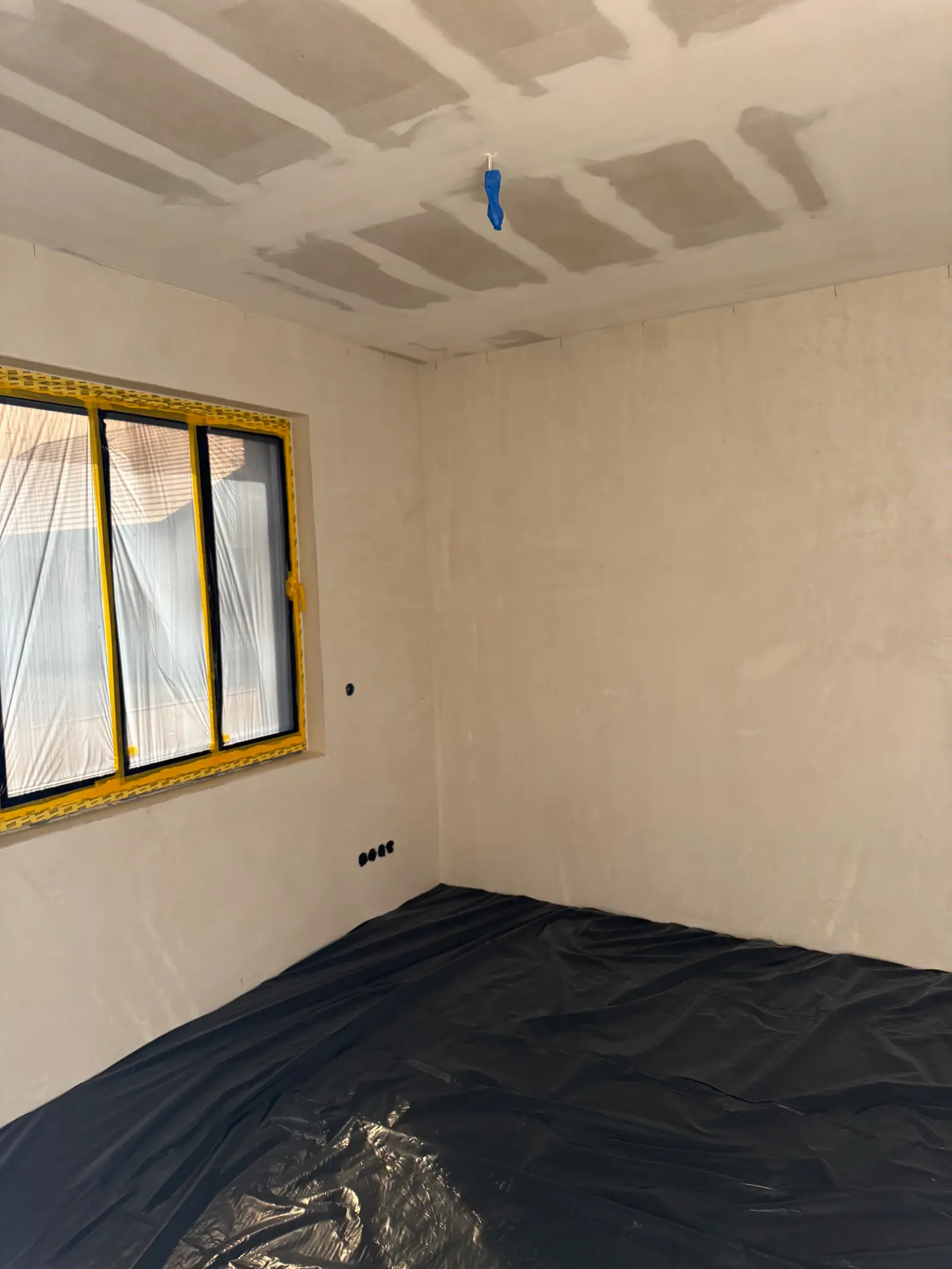 A room during the work: a window covered with film and tape, the floor covered with film.