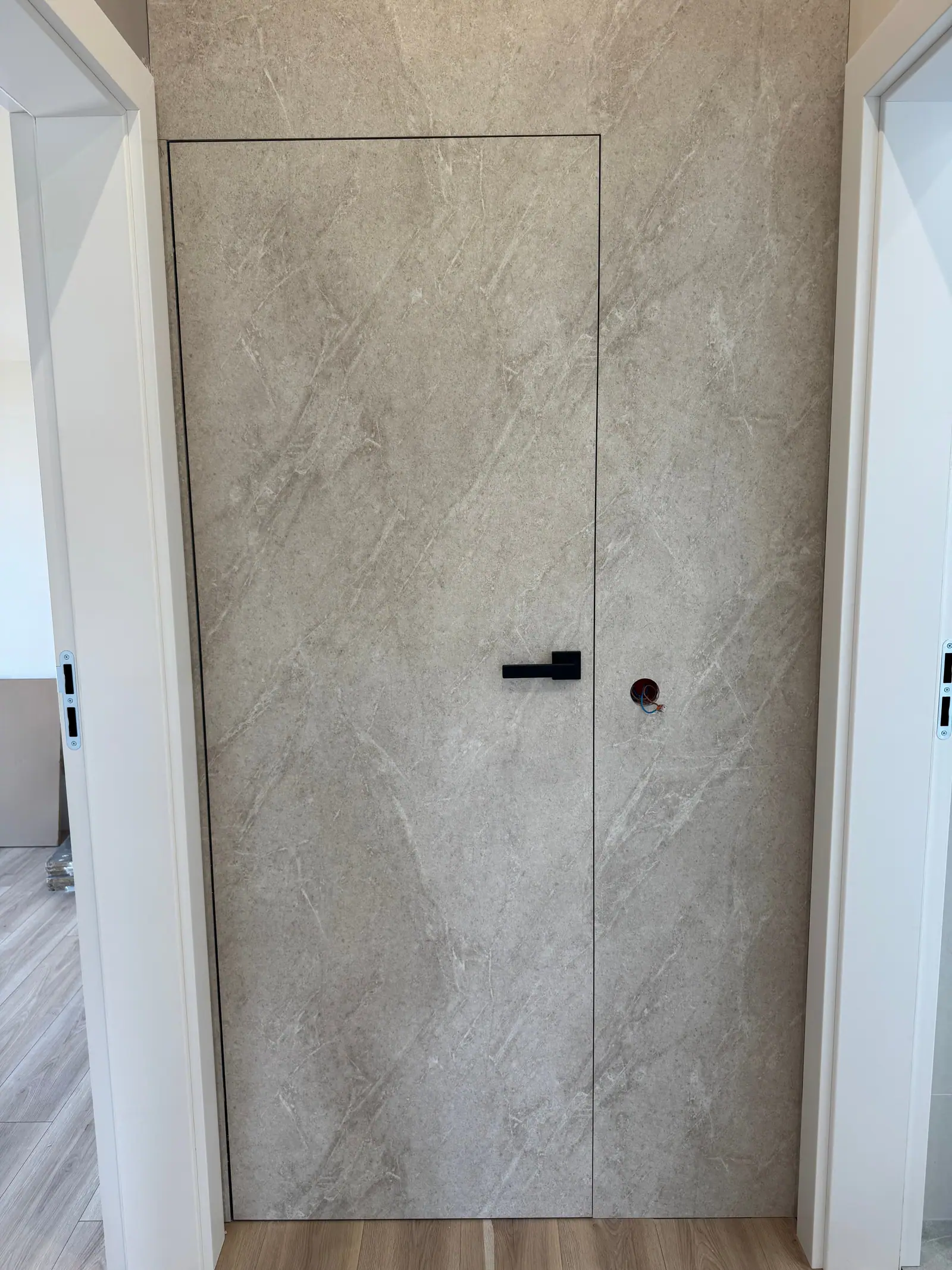 A door with a black handle set flush with the wall and covered with the same grey cladding as the wall.