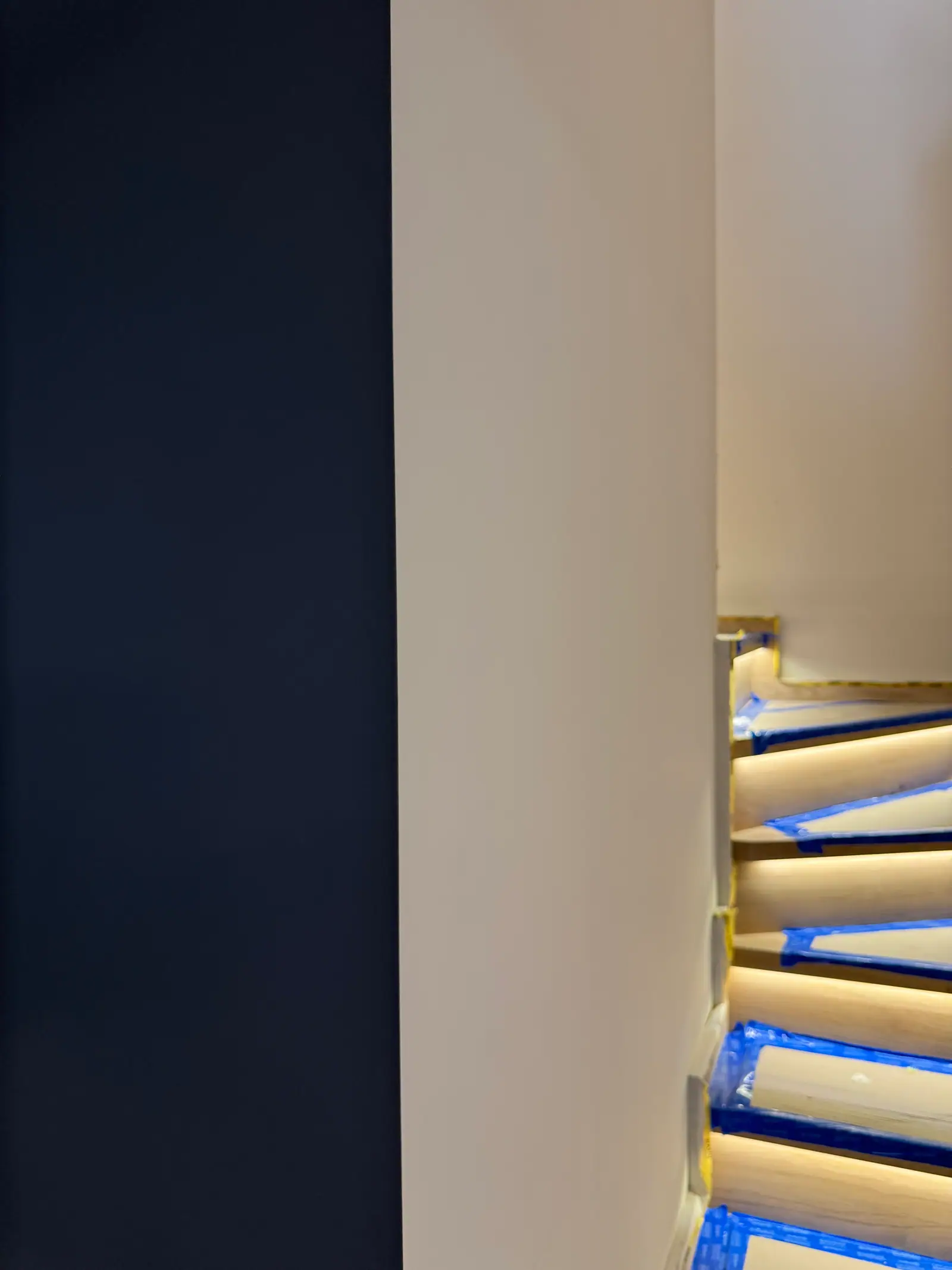 A navy wall and part of a staircase with LED lighting, the steps protected with tape during the work.