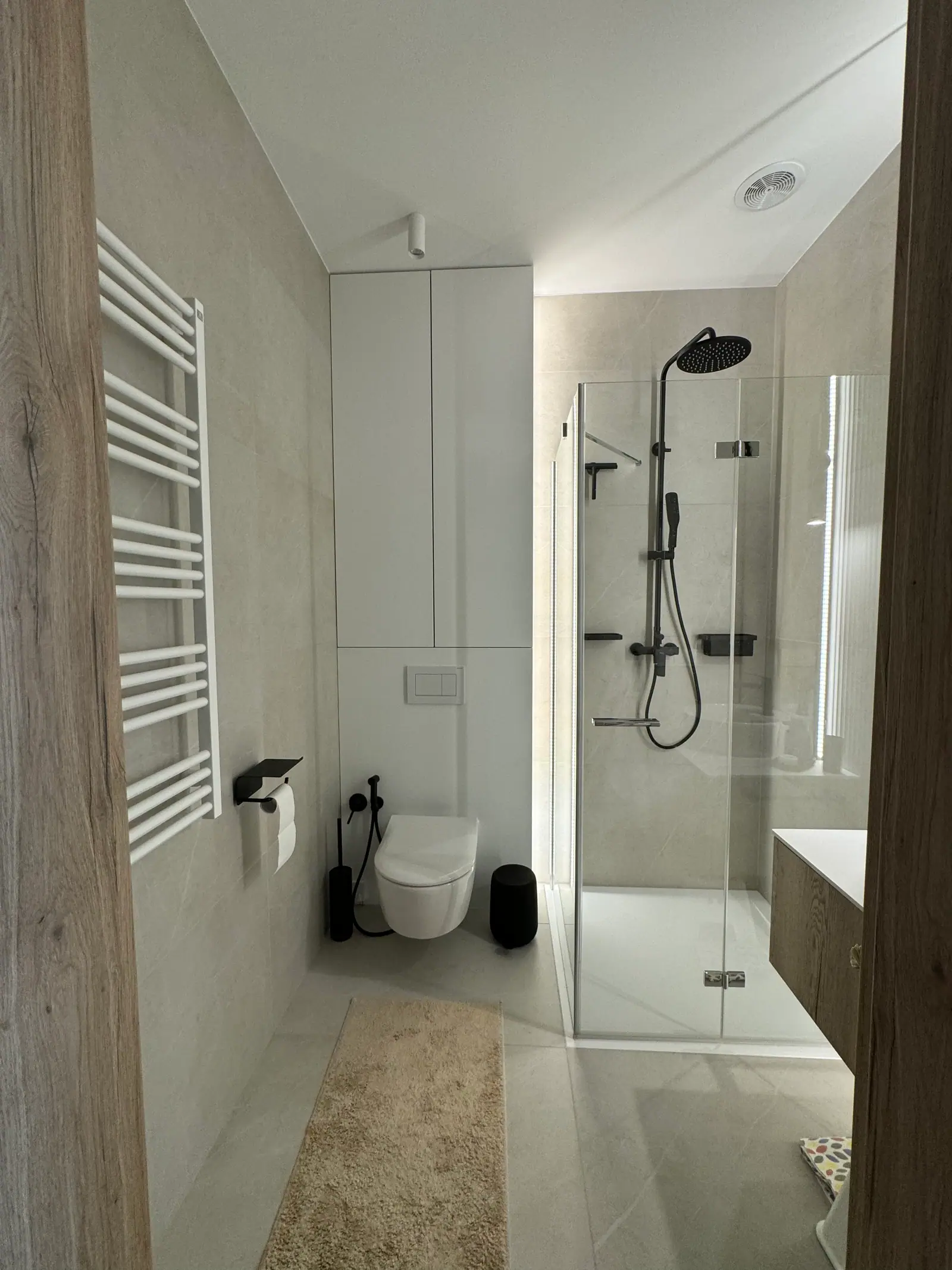 Bathroom with a shower enclosure, a wall-hung toilet, a white ladder radiator and light tiles.