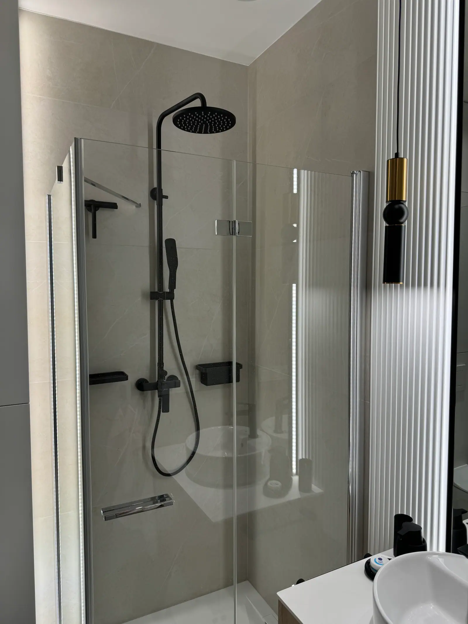 Shower enclosure with glass doors, black fittings with a rain shower head and a fluted panel beside it.