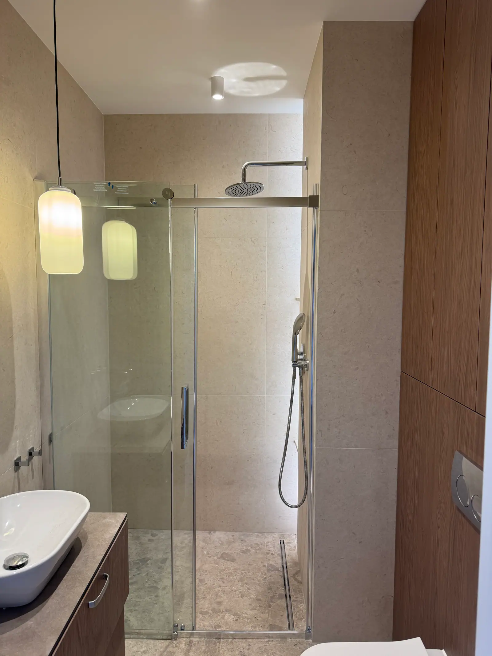 Bathroom with a shower enclosure with sliding glass doors, a countertop basin and wood-coloured built-ins.