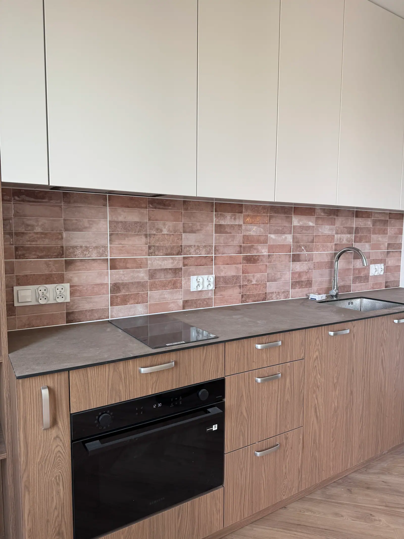 Kitchen cabinets with an oven, a hob and a sink, and brick-toned tiles above the worktop.