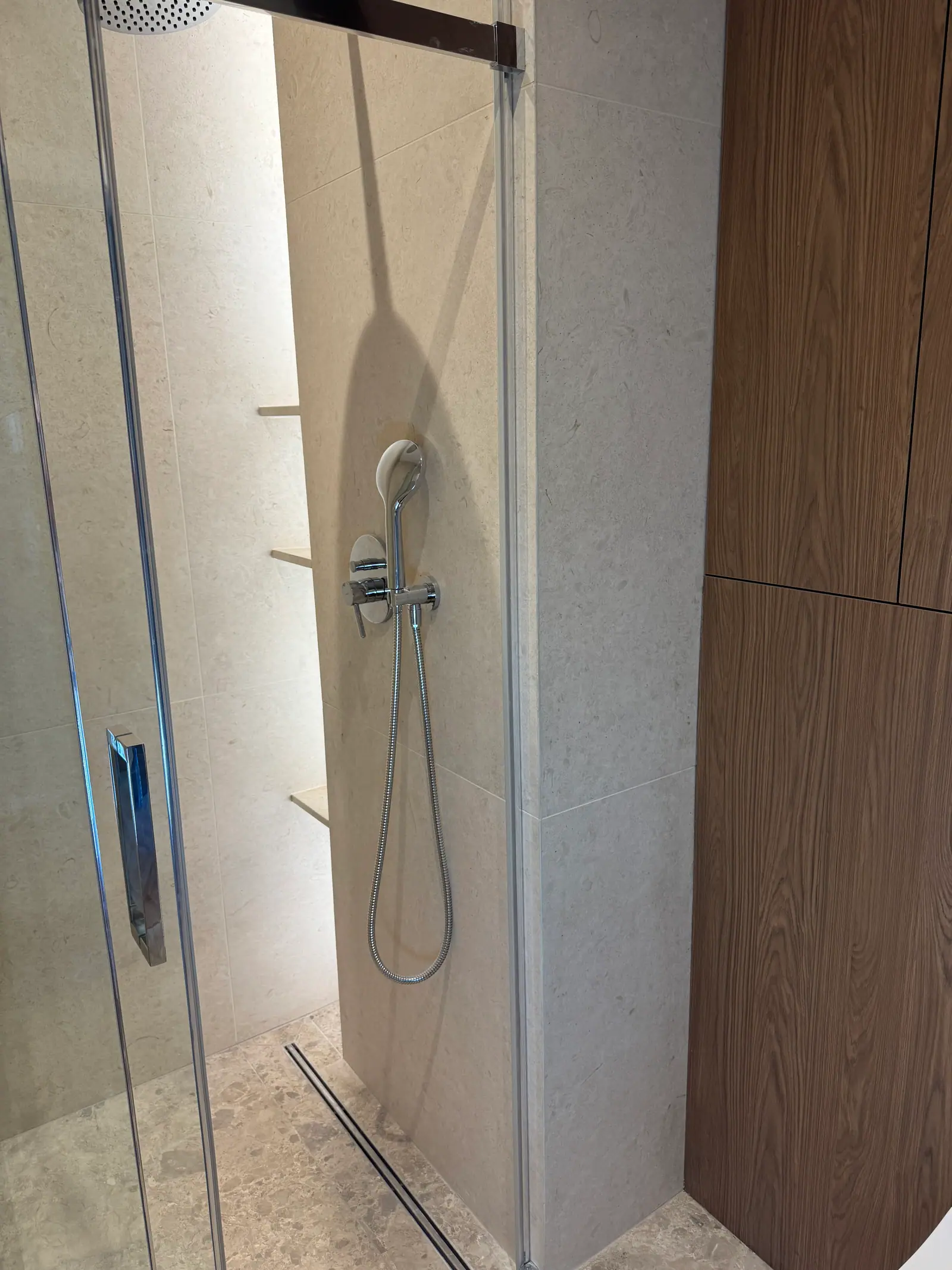 Inside the shower enclosure: a concealed mixer with a hand shower, a linear drain and a lit shelf.